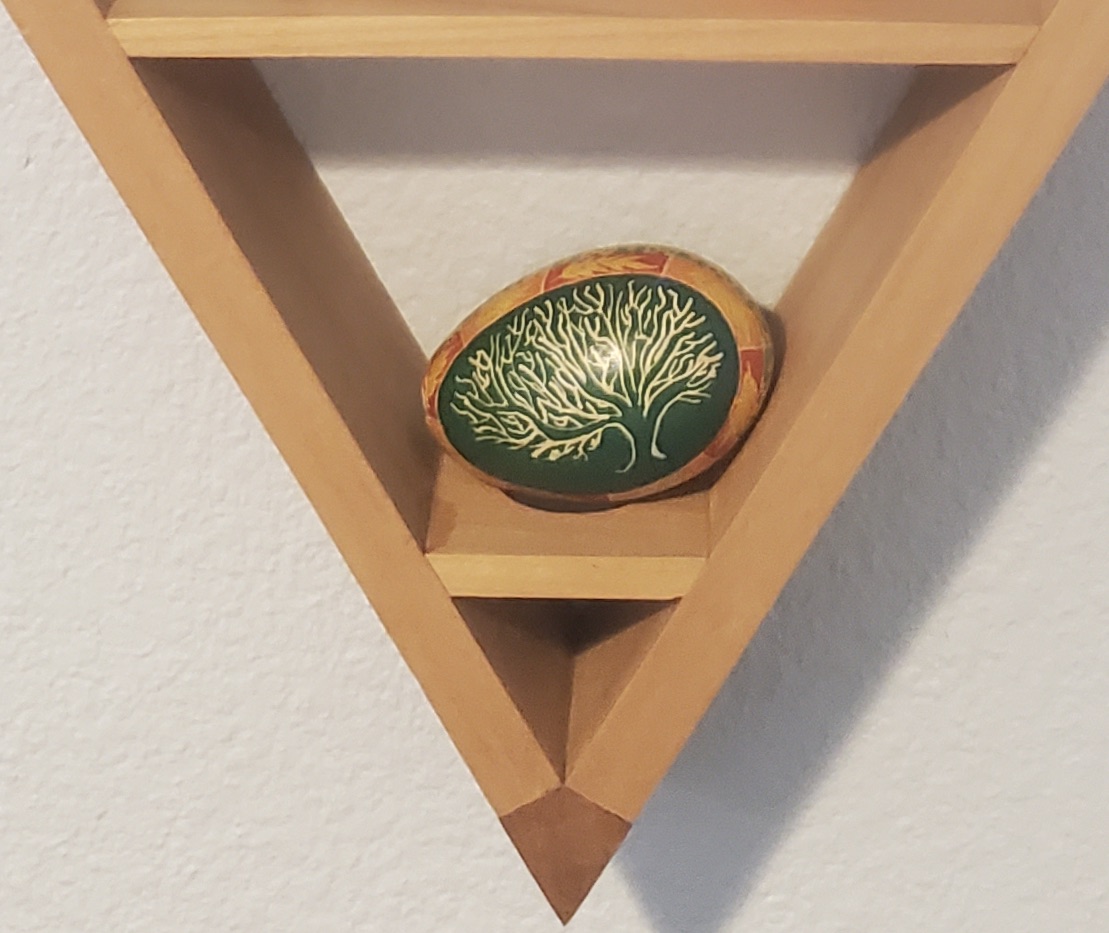 A hand-dyed easter egg with a tree on a green background sitting on a shelf