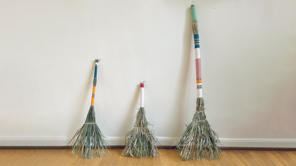 Photo of three handmade brooms leaning against a beige wall