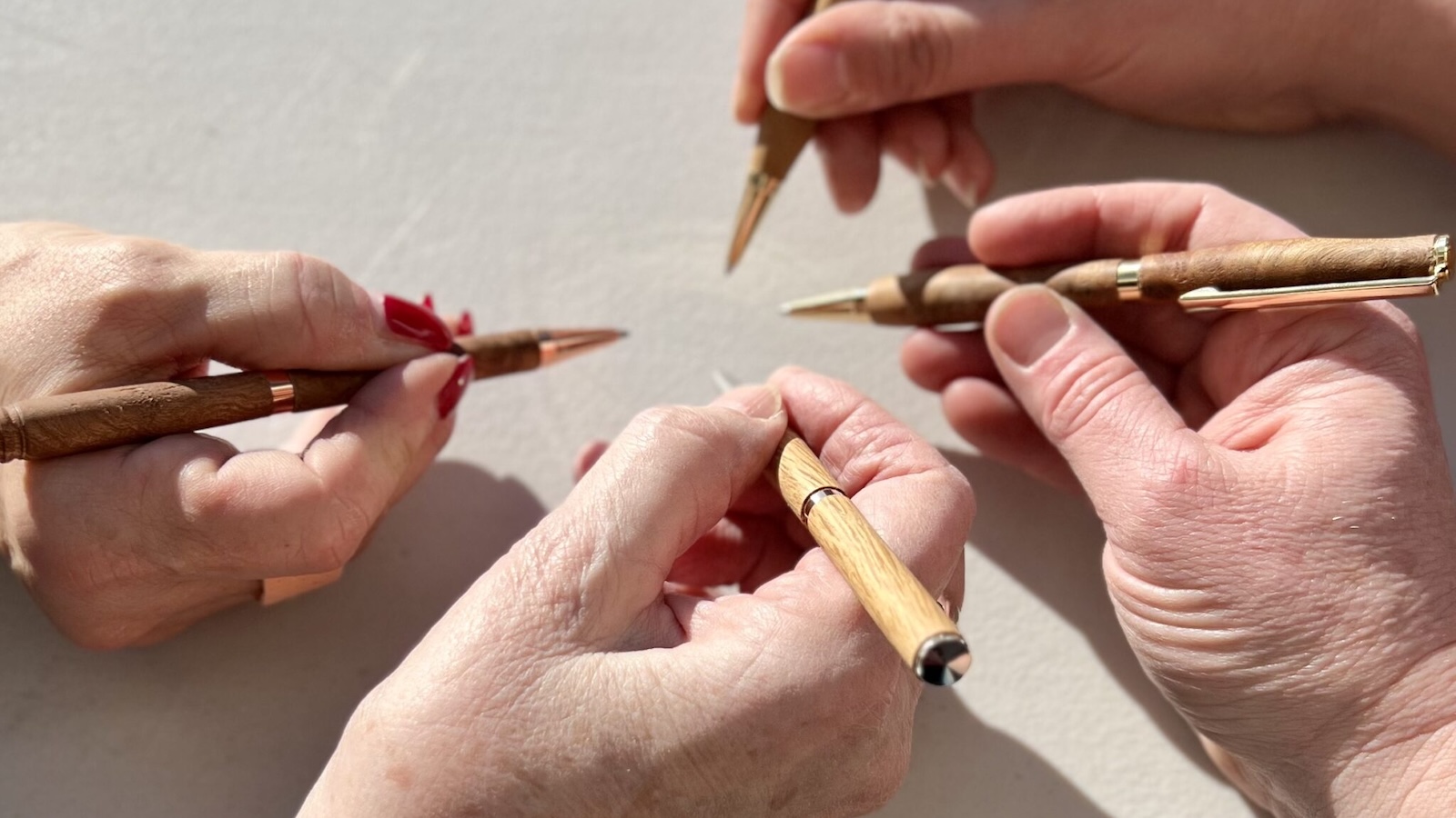 Photo of four different hands clustered together, each holding a fountain pen